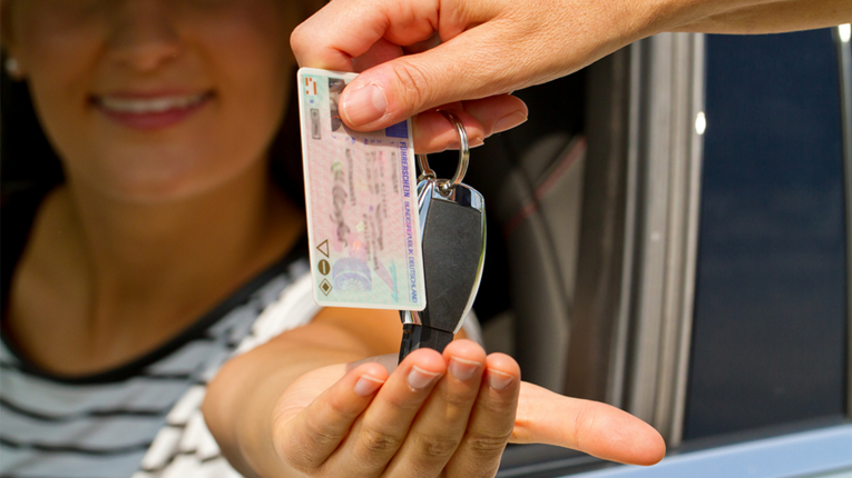 Junge Frau greift aus Auto nach Führerschein und Schlüssel