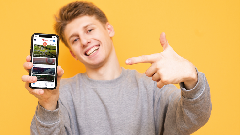 Ein Junge zeigt glücklich auf die Fahren lernen Max-App auf seinem Handy.