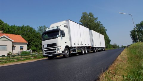 White truck drives with trailer across small road