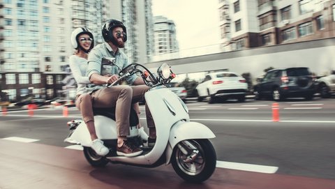 Couple drives happily together on a white scooter through the city.