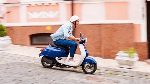 Young man driving downhill on a blue scooter over a cobblestone road.