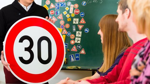 Fahrlehrer hält Straßenschild und erklärt im theoretischen Fahrunterricht 