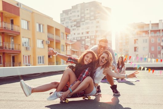 Jugendliche auf Hausdach haben Spaß auf Skateboard in der Sonne