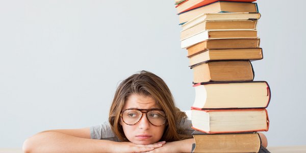 Junge Frau mit Brille gelangweilt neben Bücherstapel