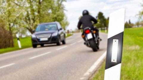 Motorrad und Auto auf Straße mit Leitpfosten