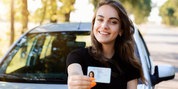 Junge Frau mit Führerschein vor Auto in Allee