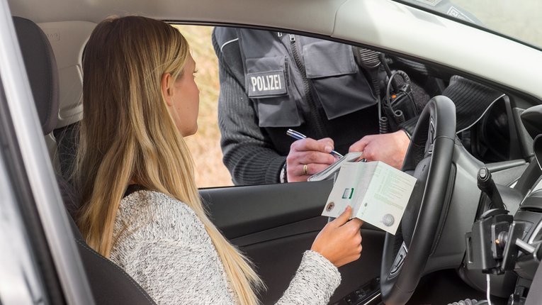 Frau zeigt Polizisten aus Auto Fahrzeugschein