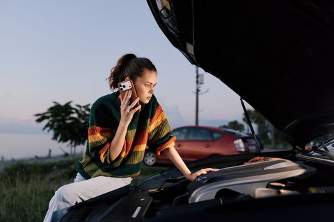 Person telefoniert nach einer Autopanne am geöffneten Motorraum.