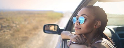Junge Frau mit Sonnebrille schaut aus Autofenster
