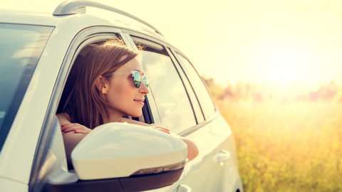 Frau mit Sonnenbrille schaut bei Sonnenschein aus weißem Auto