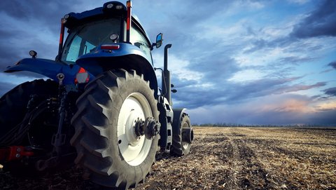 Blauer Traktor steht auf kahlem Feld.