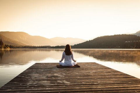Frau meditiert auf Steg an See bei Sonnenaufgang