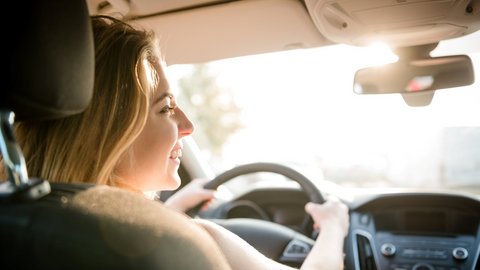 Junge Frau sitzt lächelnd hinterm Steuer im Auto